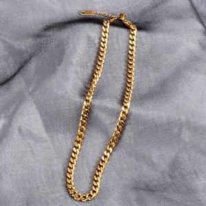 Macro detail of gold-plated cuban link chain with secure lobster clasp and extension