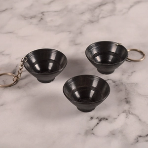 Miniature black funnel bowl keychains on marble surface shown from a 45-degree angle