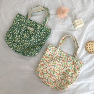 Detail of floral cotton tote bags in green and beige on a clean white fabric surface