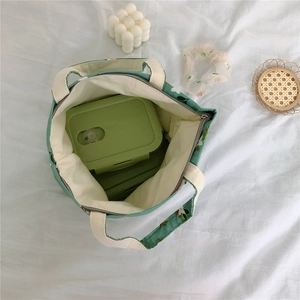 Detailed top view of a green floral lunch bag with a matching lunch box inside on a white cloth