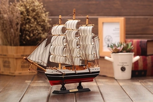 Detail of wooden sailing ship model with white striped sails and nameplate on a desk
