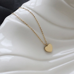 Close-up of golden heart pendant necklace on a textured white ceramic surface