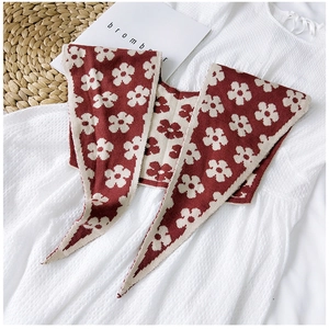 Close-up of red knitted shawl with beige floral pattern on white dress and woven mat