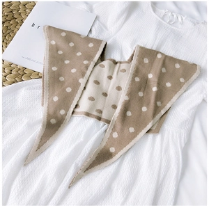 Detail of knitted khaki shawl with white polka dots on a textured white dress background
