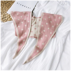 Detail of pink knitted shawl with beige polka dots on white textured fabric