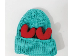 Detail of blue winter knit hat featuring chunky weave and red plush heart decorations