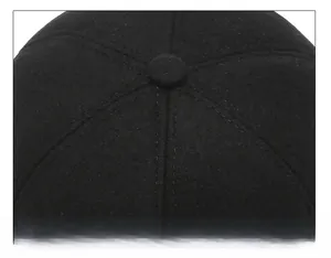Detail of the six-panel crown stitching and center button on the black wool flat cap