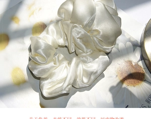 Detailed view of champagne satin scrunchie with elegant pleated silk texture and soft lighting