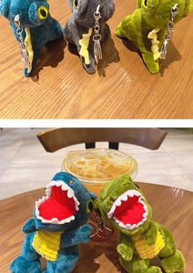 Detail of plush dinosaur keychains in blue and green with sturdy metal clips on wood