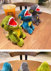 Detailed view of plush dinosaur keychains in green, blue, and gray on a wooden table