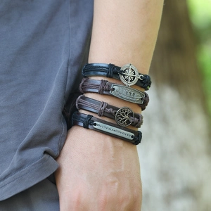 Detail of multi-layer leather bracelets featuring tree of life and compass charms