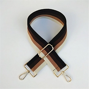 Detail of adjustable striped canvas bag strap with gold metal hardware on white background