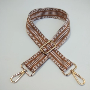 Detail of brown woven canvas purse strap with white geometric embroidery and gold hooks