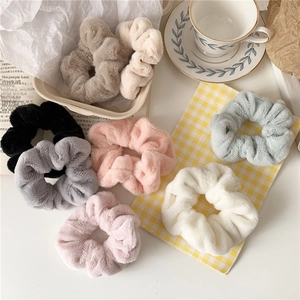 Flat lay of soft plush hair scrunchies in various pastel colors on a cozy table setting