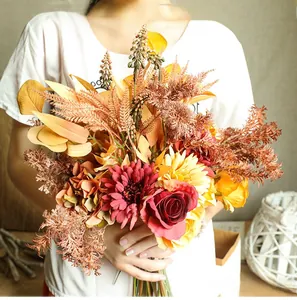 Close-up of autumn-themed silk bouquet with dark red roses and dried leaves held by hand