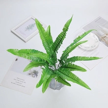 Detailed view of artificial green fern leaves in a clear glass vase on a white desk
