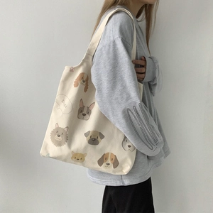 Detail view of large cream canvas tote bag with cartoon dog prints shown on model's shoulder