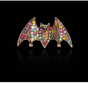 Detailed view of vintage gold bat brooch with colorful rhinestones on black background