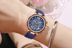 Close-up of blue leather strap watch with rose gold case and Roman numeral dial details