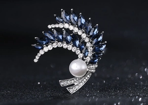 Detailaufnahme einer silbernen Brosche mit blauen Edelsteinen und einer großen Perle