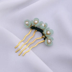 Detailed close-up of golden U-shaped hair fork with green flowers and white pearls
