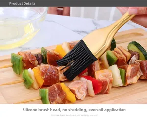 Dettaglio del pennello in silicone con manico dorato che spennella olio su spiedini di carne