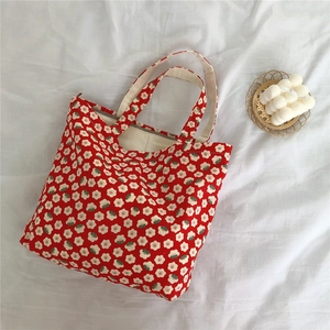 Close-up of red floral cotton canvas handbag on white fabric with decorative candle