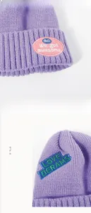 Detail view of purple knitted beanie showing pink and teal embroidered letter patches