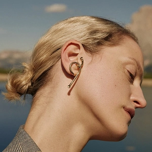 Minimalist gold sculptural ear cuff with fluid metal lines shown on a model outdoors