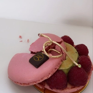 Detailed close-up of a gold curved ear cuff with pink and green gems on a macaron