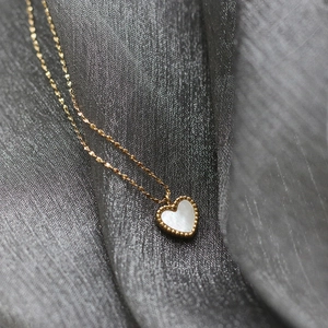 Macro shot of gold-plated heart pendant with white mother of pearl inlay on silk