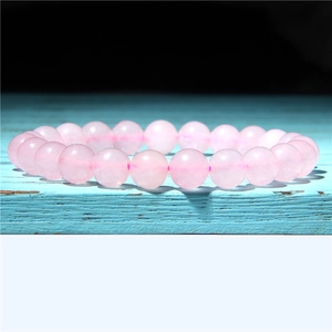 Close-up of natural rose quartz beaded bracelet on a blue wooden surface with black backdrop