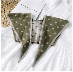Detail of green knitted shawl with beige polka dots on a natural straw mat background