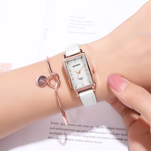 Close-up of a rectangular rose gold quartz watch with a white leather strap on a wrist
