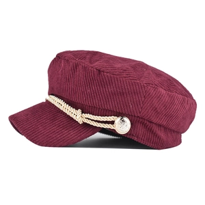 Detail of burgundy corduroy baker boy hat featuring golden rope and metallic buttons