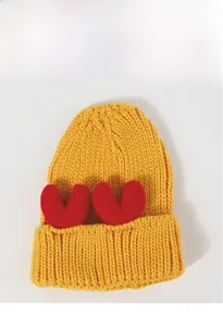 Close-up of a yellow chunky knit beanie featuring two cute red plush heart ornaments