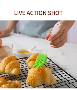 Close-up of a green silicone brush applying oil to a fresh croissant on a cooling rack