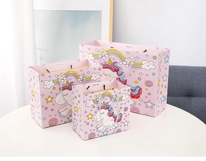 Three sizes of pink unicorn paper gift bags with rainbow patterns and silver rope handles