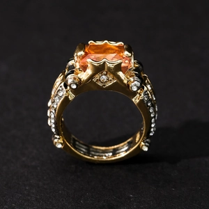 Detail view of gold-tone ring featuring a square orange gemstone and pave-set side stones