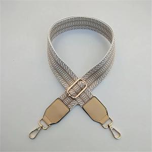 Detail of adjustable woven wide shoulder strap with beige geometric pattern and gold hooks