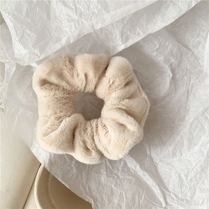 Close-up of soft plush scrunchie in beige faux fur on an aesthetic book background