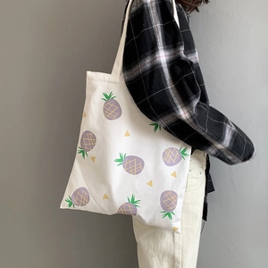 White canvas tote bag featuring a purple pineapple print worn on a model's shoulder