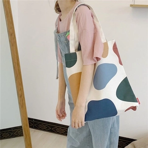 Close-up of canvas tote bag featuring artistic colorful patterns and woven strap on model