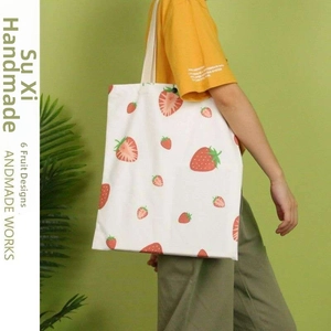 Detail view of a white canvas tote bag with vibrant strawberry print patterns and sturdy straps