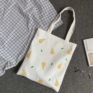 Detailed flat lay of a beige canvas tote bag with yellow pear print and lifestyle props
