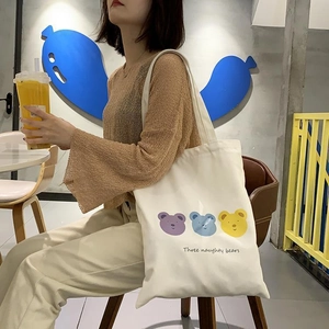 Detail of white canvas tote bag featuring three colorful bears in a cozy cafe setting