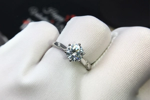 Macro shot of silver six-prong moissanite ring with side diamonds on a gloved finger