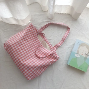 Detail of pink gingham canvas tote bag with dual handles on white textured backdrop