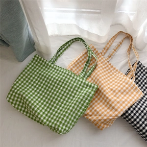 Three Gingham cotton tote bags in green, yellow, and black colors on a bed