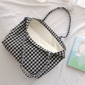 Flat lay of large black and white checkered canvas tote bag with books on white fabric